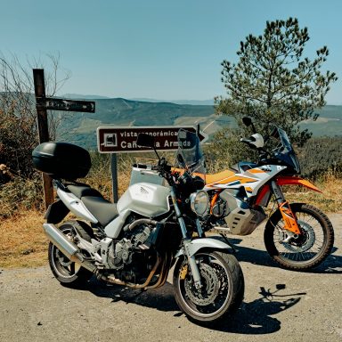 Dos motos estacionadas junto a un cartel que indica dirección en un paisaje montañoso.