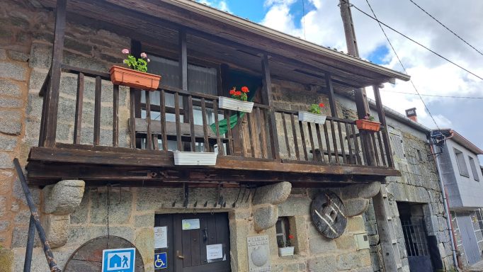 Balcón de casa de piedra con macetas de flores y cielo nublado.
