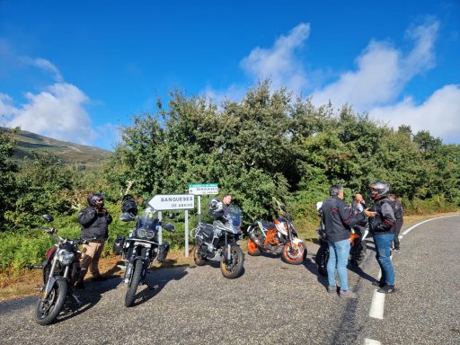 Grupo de motociclistas deteniéndose junto a una señal en una carretera rural.