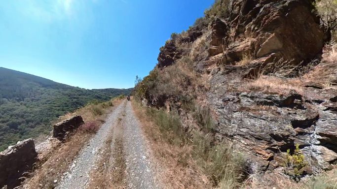 Sendero de tierra junto a un acantilado y vistas verdes en un día soleado.