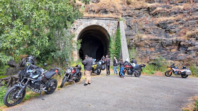 Grupo de motociclistas cerca de un túnel en un paisaje montañoso.
