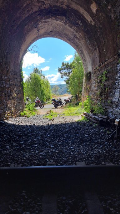 Vista desde un túnel de tren, con luz natural y vegetación al fondo.