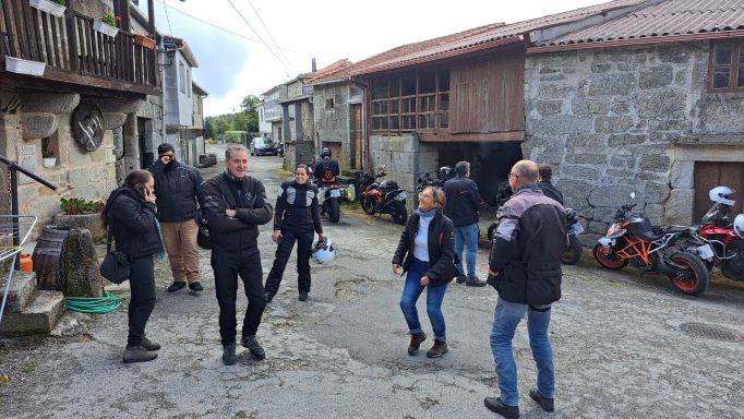 Grupo de personas conversando en una calle de un pueblo rural, rodeados de edificios de piedra.